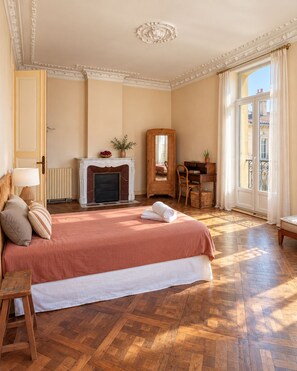 A hotel room with a large bed, a fireplace, a desk, and a view of the city. - Maison Sarava – Charming apartment with balconies and spacious rooms (Espira-de-l'Agly)