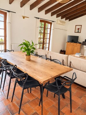A dining area with a wooden table and black chairs, a potted plant, and a sofa in the background. - Maison Sarava – Charming apartment with balconies and spacious rooms (Espira-de-l'Agly)
