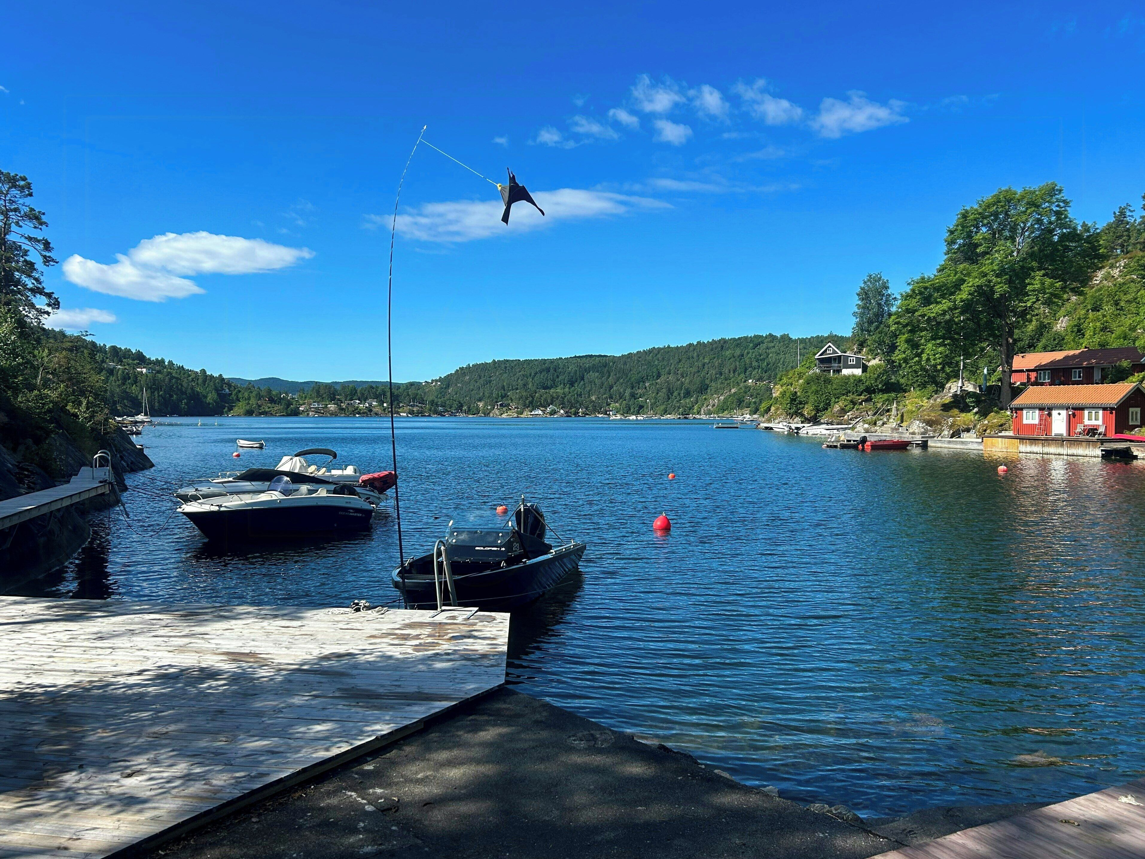 Un lac paisible où des bateaux sont amarrés à un quai, entouré de collines boisées et d’un bâtiment rouge.