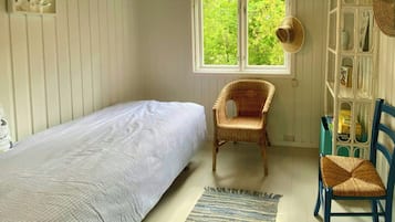 Une chambre comprenant un lit simple, une chaise, une petite table, une fenêtre donnant sur un espace verdoyant et une étagère contenant divers objets.