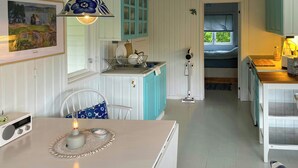A compact kitchen with white and teal cabinetry, a dining area with a table and chairs, and a visible bed in the adjacent room.