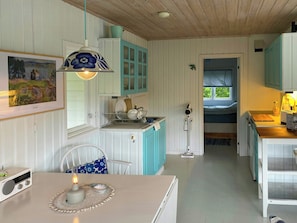 A compact kitchen with white and teal cabinetry, a dining area with a table and chairs, and a visible bed in the adjacent room.