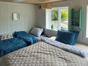 A bedroom with a bed, two pillows, a bedside table, a window with a view, and a hanging light fixture.