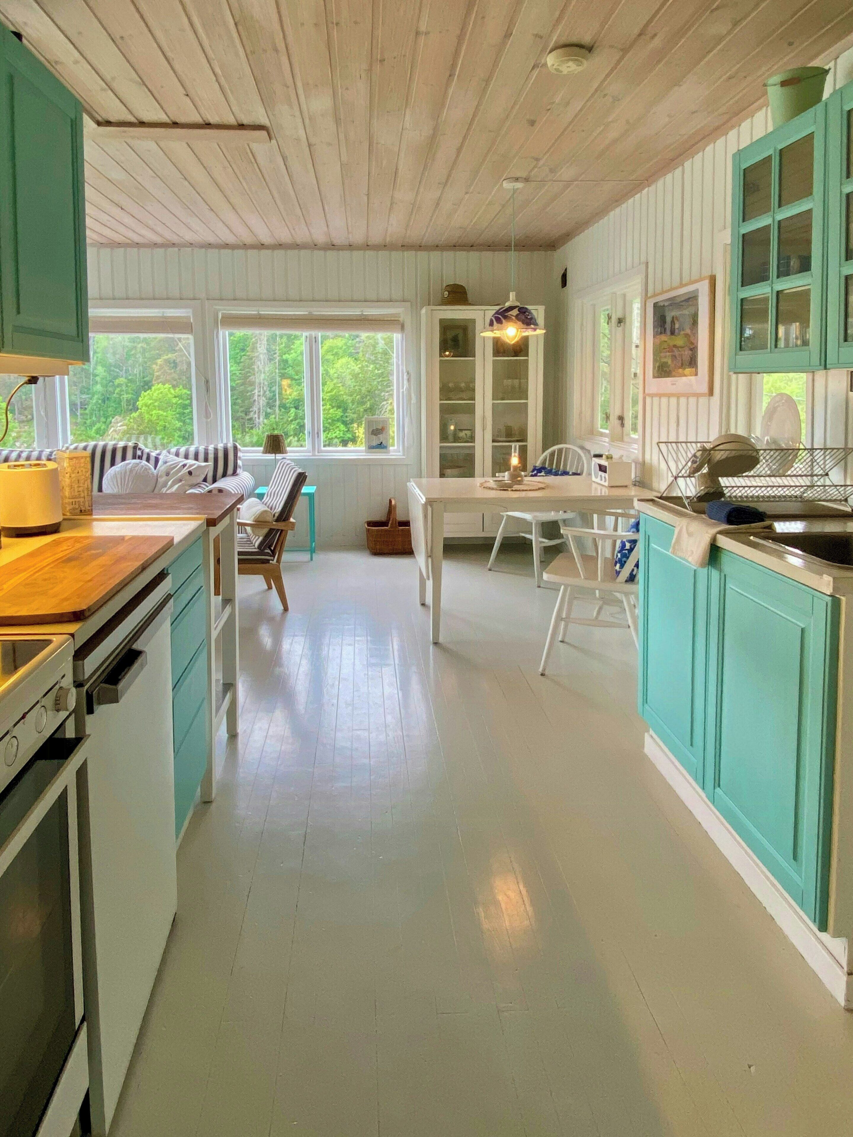 Une cuisine avec des meubles en bois, une table à manger et une vue sur l’extérieur grâce à de grandes fenêtres.