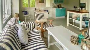 A cozy living room with a striped sofa, a wooden chair, a white table, and a kitchen area with teal cabinets.