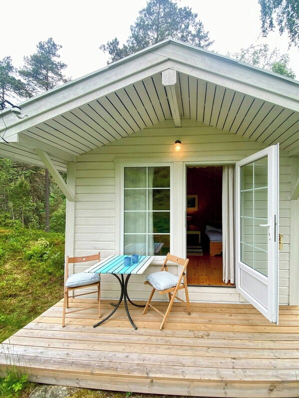 A wooden deck with a table and chairs, a covered porch, and a view of a forested area.