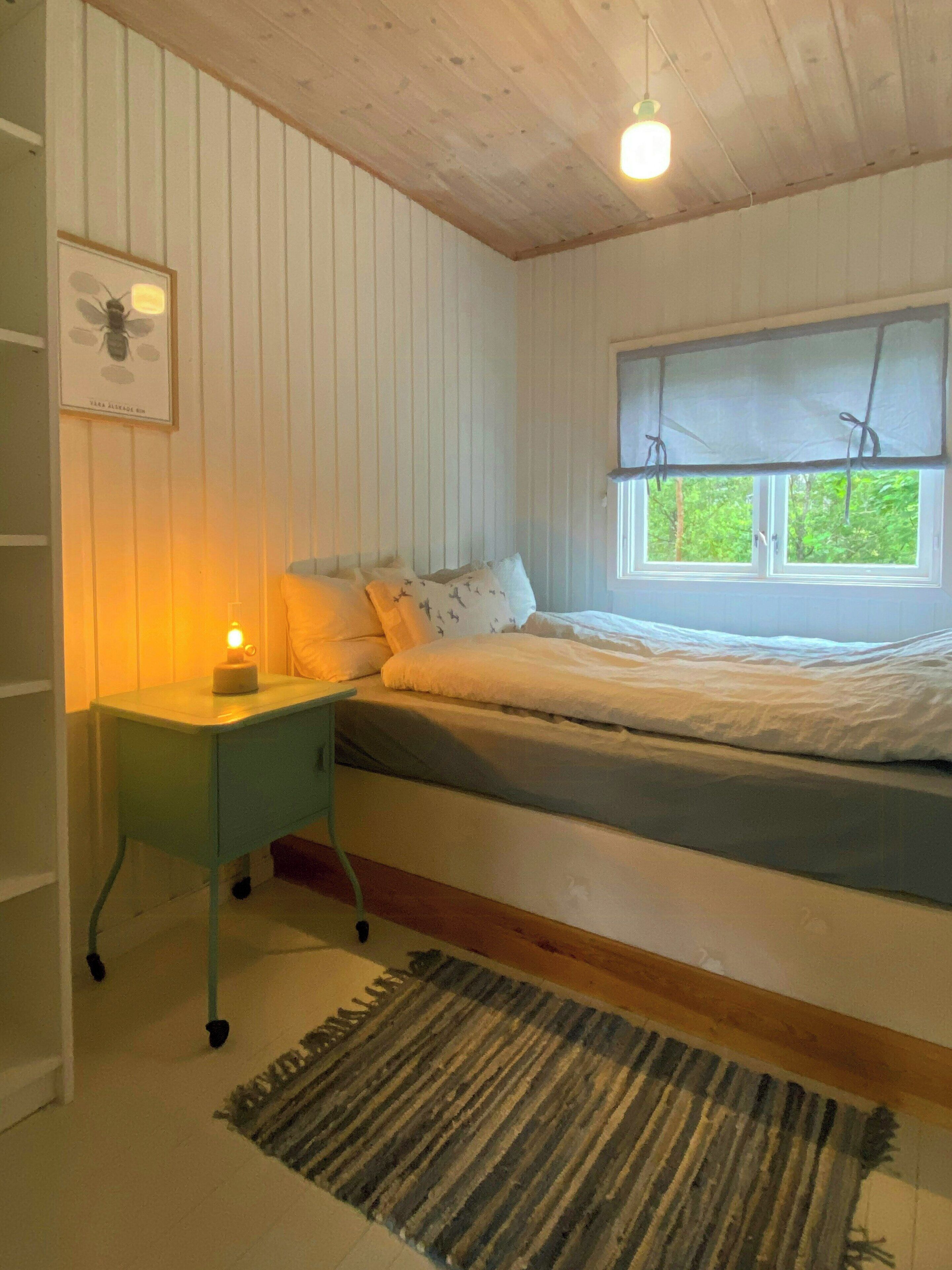 Ein Schlafzimmer mit Bett, Nachttisch, Lampe, Fenster und Teppich.