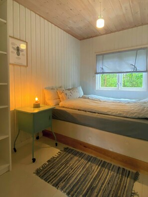 A bedroom with a bed, bedside table, lamp, window, and a rug. - Waterside cabin with boat slips on the Oslofjord (Akershus)