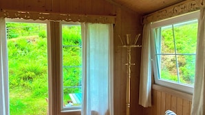 A wooden room with a bed, a window, and a view of greenery outside.
