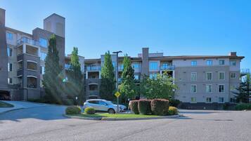 A multi-story residential building with balconies, a parking area, and well-maintained landscaping.