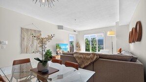 A modern living room with a glass dining table, a sofa, and a TV displaying a beach scene.