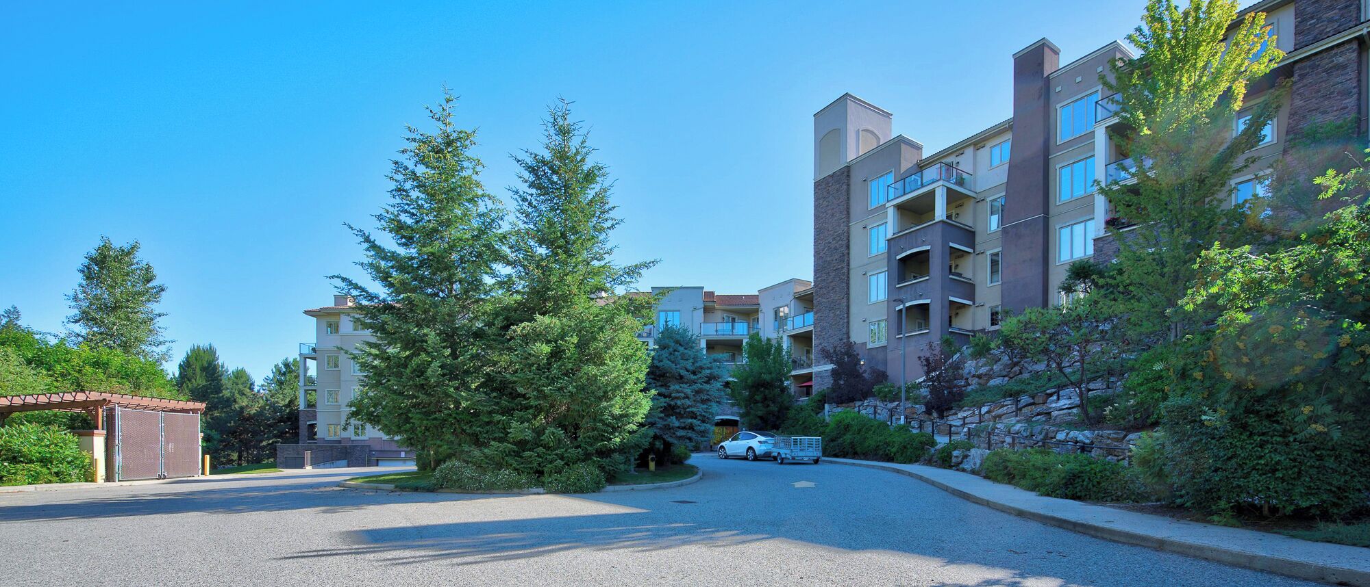 A residential area with multi-story buildings, a gated entrance, and a car parked in the driveway.