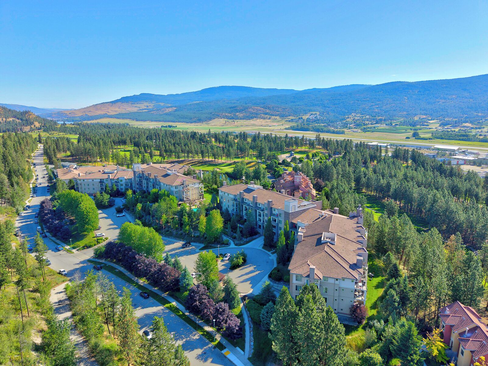 A residential area with multiple apartment buildings, a parking lot, and a golf course in the background.