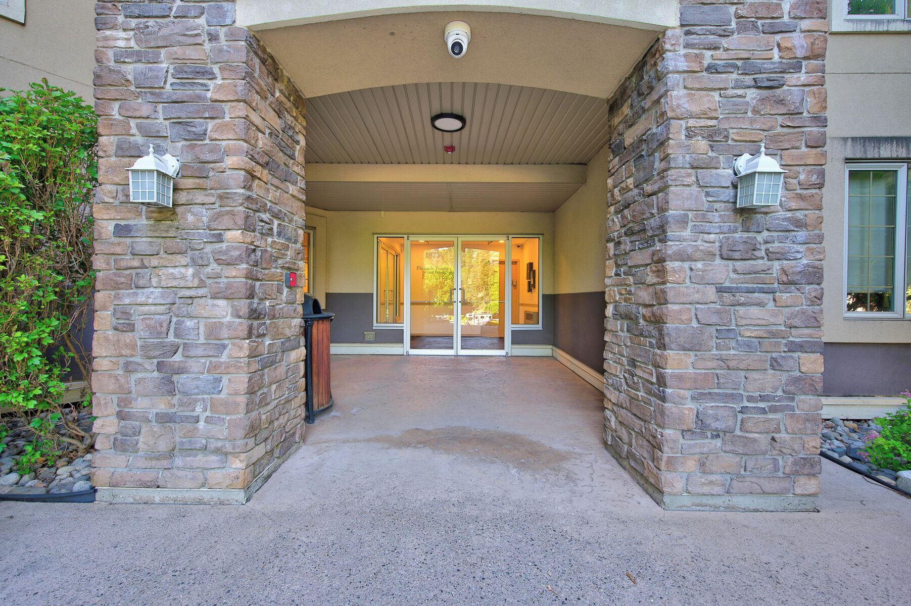 A stone entrance with glass doors, a security camera, and a fire alarm.