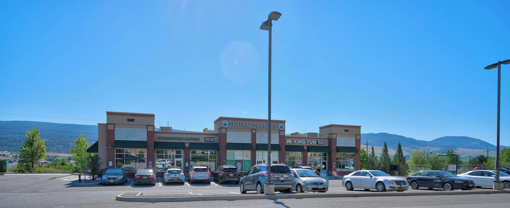 Un estacionamiento con coches, una cafetería Starbucks, una tienda Central Cannabis y una tienda Xing Yun.