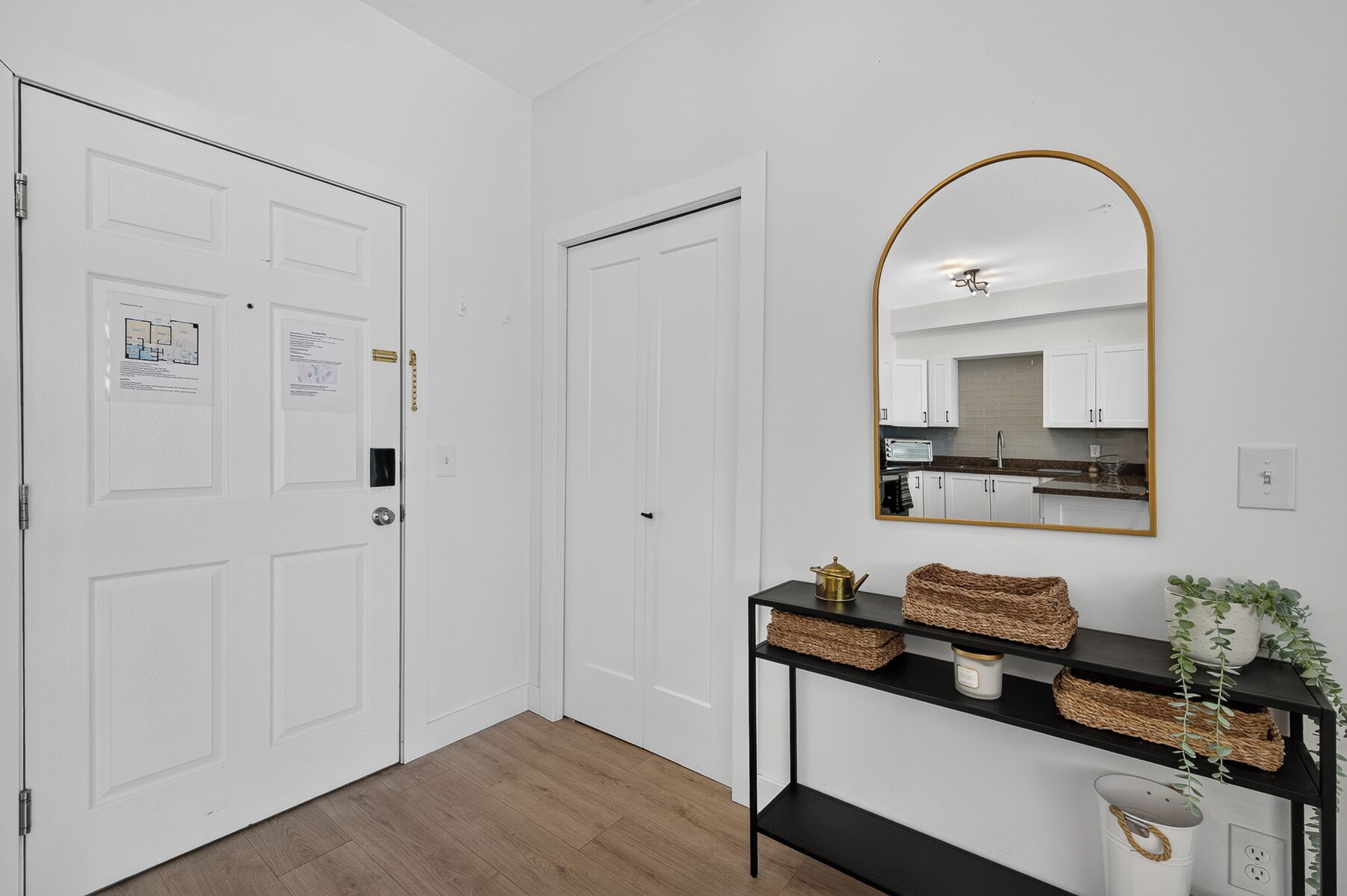 A hallway with white doors, a black console table with baskets, a mirror, and a kitchen visible through an open door.