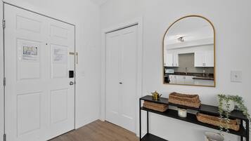 A hallway with white doors, a black console table with baskets, a mirror, and a kitchen visible through an open door.
