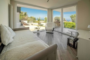 A bedroom with a large bed, a chair, a desk, and a view of the outdoors. - Sunlit gulffront villa with pool (Carini)