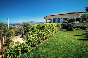 A residential property with a well-maintained garden, a paved driveway, and a view of the sea and mountains in the background. - Sunlit gulffront villa with pool (Carini)
