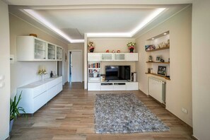A modern living room with a flat-screen TV, built-in shelving, and a grey rug. - Sunlit gulffront villa with pool (Carini)