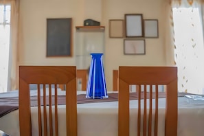 A dining area with two wooden chairs, a table, a blue vase, and framed pictures on the wall. - Hillside Hideaway mountain villa with views, shared terrace, and private garden (Skiadas)