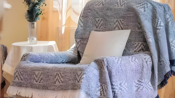 Ein Zimmer mit einer Couch, einem kleinen Tisch mit einer Vase und durchsichtigen Vorhängen.