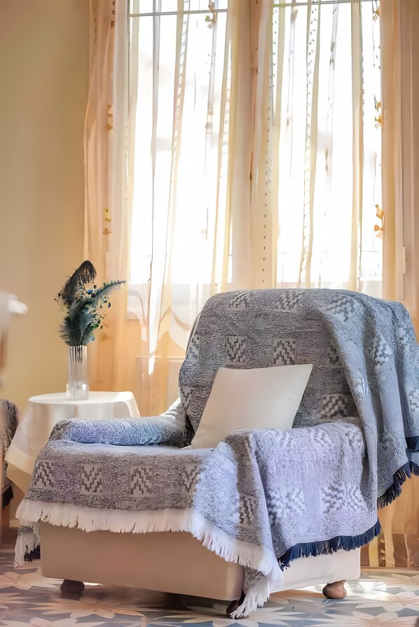 A room with a sofa, a small table with a vase, and sheer curtains.