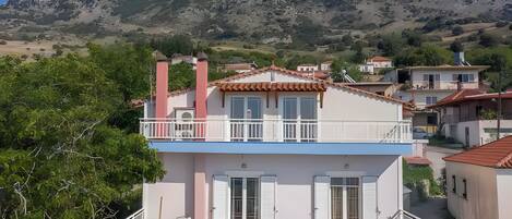 A two-story building with a balcony, a chimney, and a view of a mountainous landscape.