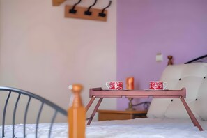 A bed with a headboard, a bedside table with a candle, and a tray with two cups.