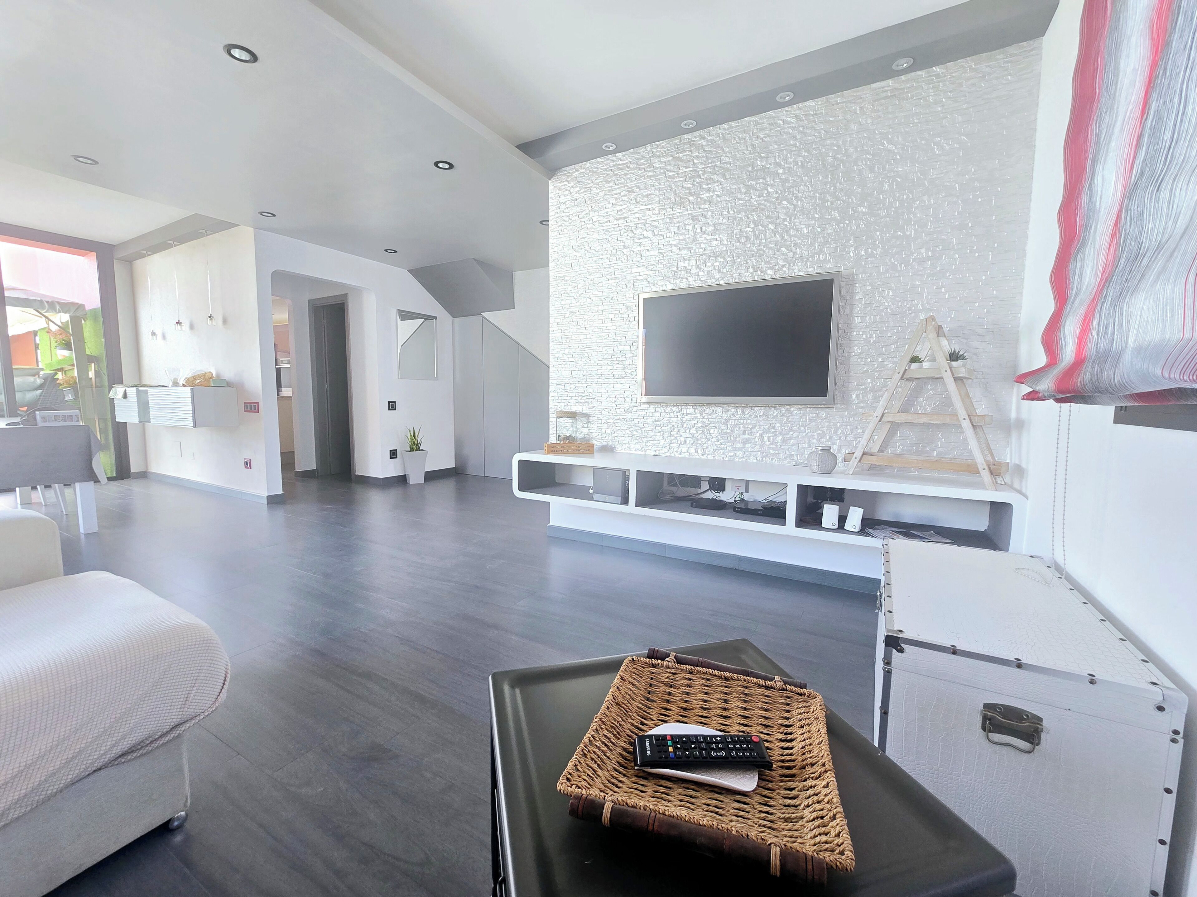 Een moderne woonkamer met een flatscreen televisie bevestigd aan een gestructureerde muur, een bank en een salontafel met een afstandsbediening.
