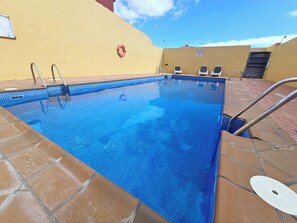 Ein Schwimmbecken mit gefliesten Rändern, einem Rettungsring und einigen Liegestühlen.