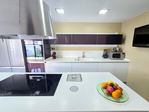 A modern kitchen with a black induction cooktop, a microwave, and a fruit bowl on the counter. - Oasis House (Maspalomas)