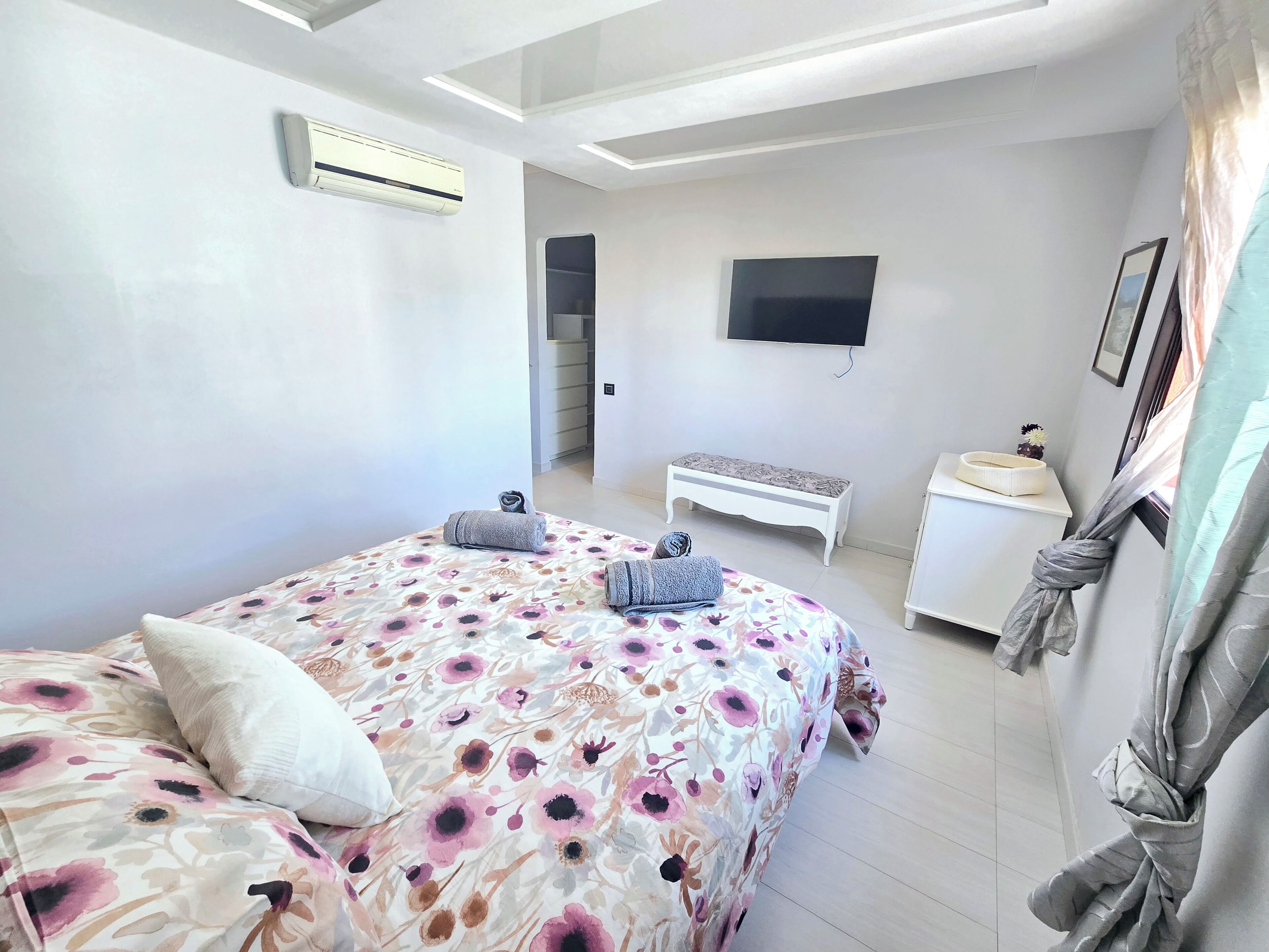 Een moderne slaapkamer met een bed, een bankje, een televisie en een nachtkastje.