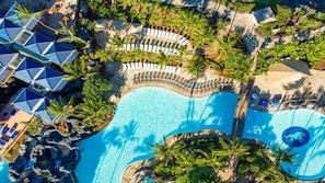 Eine Luftaufnahme eines Resorts mit großem Pool, Liegebereichen und Palmen.