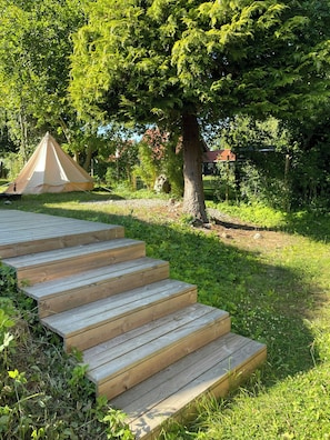 Eine Holztreppe führt zu einem Zelt auf einer grünen Wiese mit Bäumen.