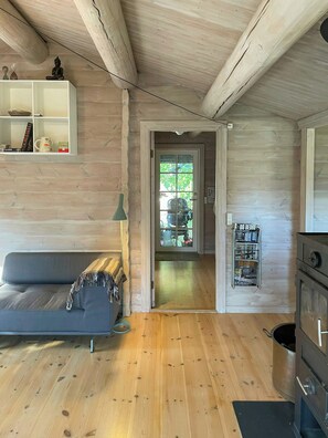Ein gemütliches Blockhaus-Interieur mit Holzboden, einer Couch, einem kleinen Tisch mit Dekoration, einer Tür zu einem Balkon und einer Küchenzeile mit Herd.