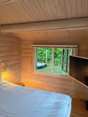 A cabin room with a bed, a lamp, a television, and a window with a view of greenery. - Beamed house by the water in Hornbæk (Hornbæk)