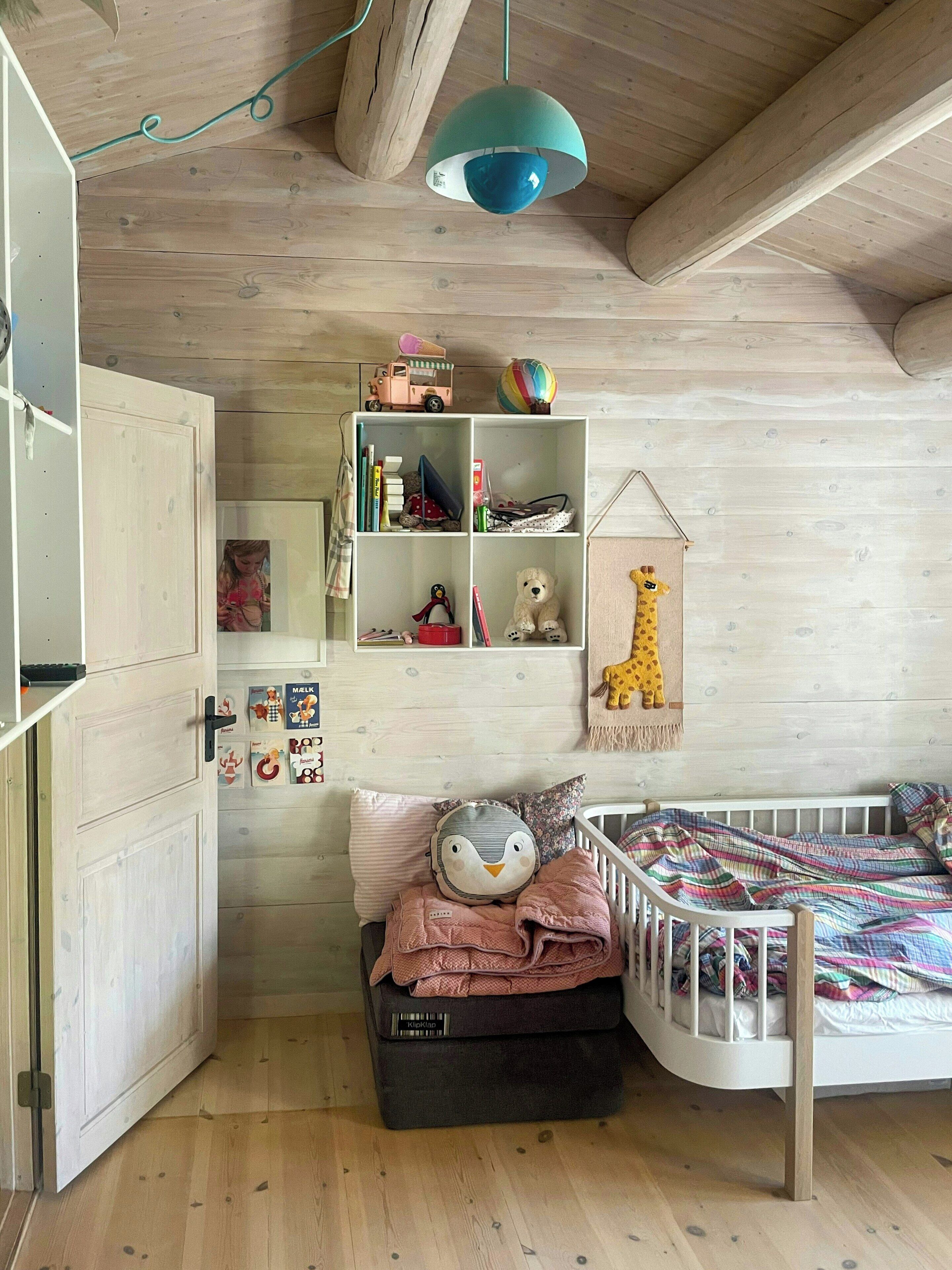 A child's room with a crib, a shelf with toys, and a hanging giraffe decoration.