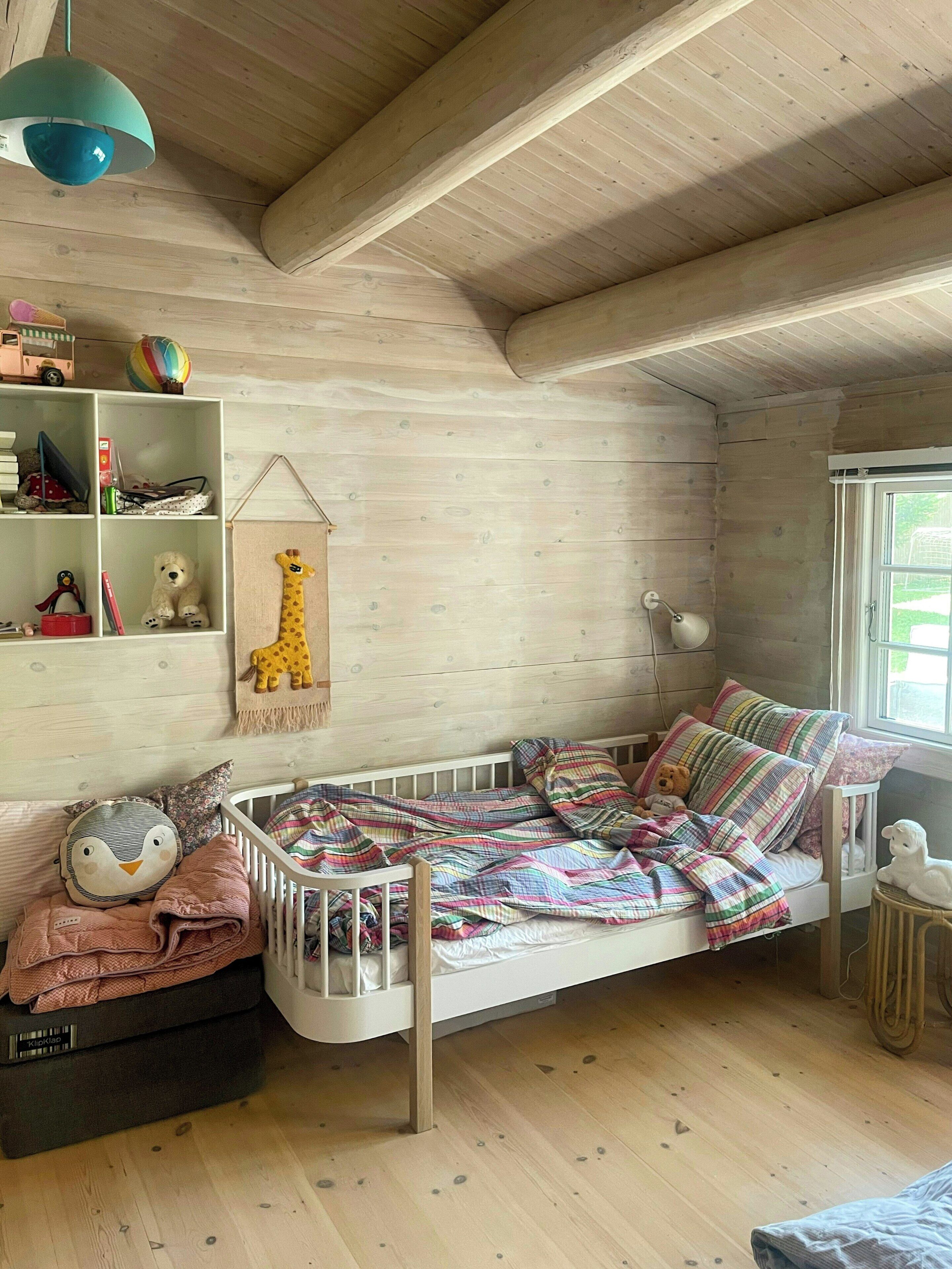 Une chambre d’enfant accueillante, avec un lit superposé, une bibliothèque et une décoration représentant une girafe suspendue.