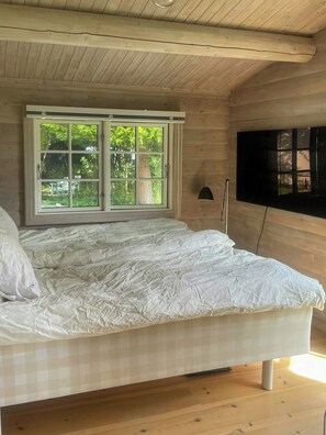 Ein Schlafzimmer mit einem großen Bett, einem Fenster mit Blick ins Grüne und einem an der Wand montierten Fernseher.