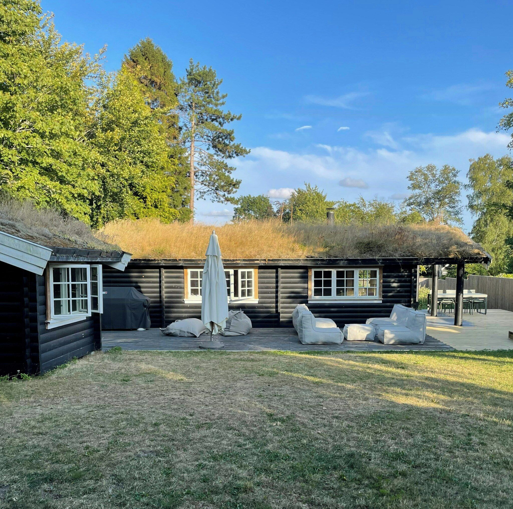 Une cabane en rondins avec un toit de chaume, un espace extérieur aménagé pour s’asseoir et une cour clôturée.