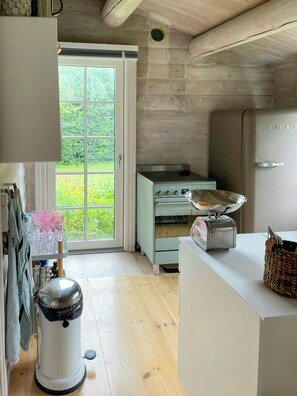 Uma cozinha com teto de madeira, janela com vista para vegetação, torradeira antiga e geladeira branca.