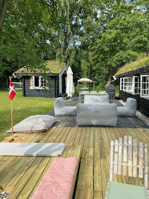 A wooden deck with outdoor seating, a flag, and a small cabin. - Beamed house by the water in Hornbæk (Hornbæk)