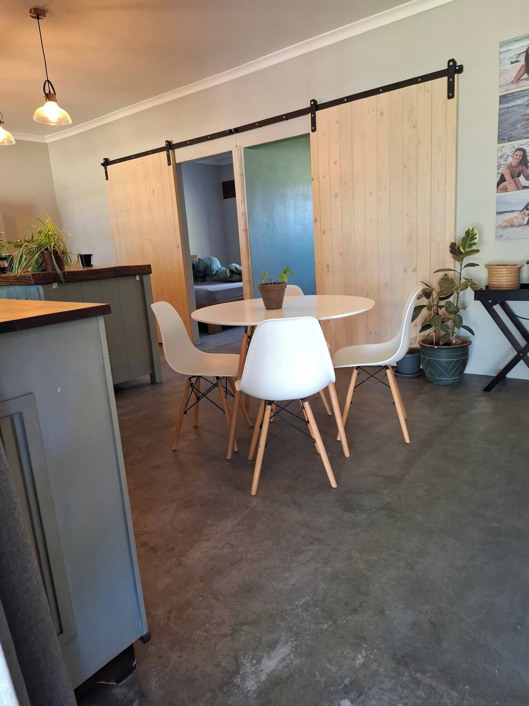 A modern dining area with a round table and white chairs, a wooden counter, and a sliding barn door.