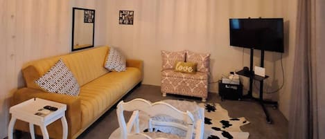 Uma sala de estar com sofá, poltrona, televisão e luminária no teto.
