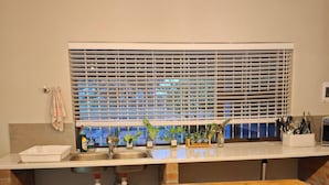 Uma cozinha com bancada de madeira, pia, janela com persianas e luminária pendente.