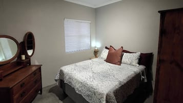 A bedroom with a bed, dresser, mirror, window, and ceiling light.
