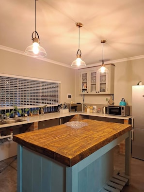 A kitchen with a central island, overhead pendant lights, a microwave, a toaster, and a refrigerator. - Rustic Farmhouse Retreat in Cape Winelands, South Africa (Paarl)