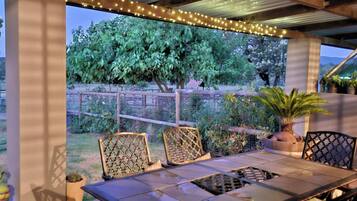 An outdoor patio with a table and chairs, surrounded by plants and a fence.
