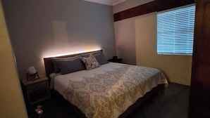 Quarto com cama, mesa de cabeceira e janela com persianas.